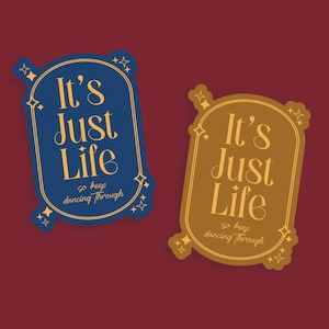 May include: Two stickers with the text "It's Just Life" in a vintage font. One sticker is navy blue with gold accents, and the other is a mustard yellow color with gold accents. The stickers have a decorative border and the phrase "so keep dancing through".