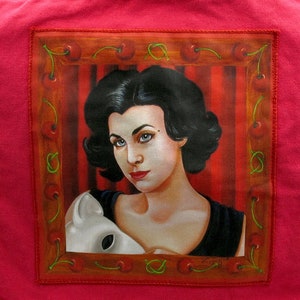 Puede incluir: Una bolsa de lona rosa con una imagen enmarcada de una mujer con cabello oscuro sosteniendo una máscara blanca. La imagen está rodeada de un marco rojo y marrón con cerezas.