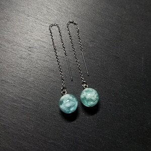 Peut inclure: Une paire de boucles d'oreilles pendantes argentées avec une boule de résine nuageuse bleu clair et blanc au bout de chaque chaîne.