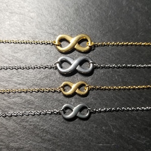May include: Four infinity symbol necklaces, two gold and two silver, on a dark grey background.