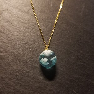 Peut inclure: Un collier en chaîne dorée avec un pendentif en verre bleu contenant des nuages blancs.