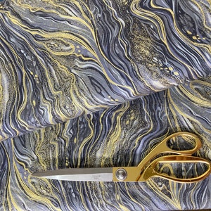 May include: Black fabric with a gold and silver marbled pattern. A pair of gold scissors is lying on top of the fabric.