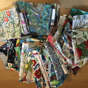 May include: A collection of colourful fabric scraps in various patterns and textures. The fabrics are arranged in a pile on a wooden surface.