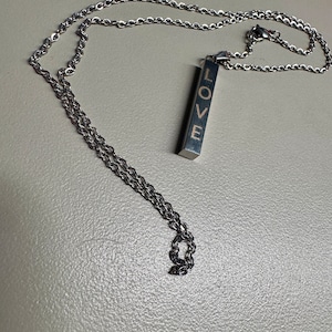 May include: A silver chain necklace with a silver bar pendant that says "LOVE" in gold lettering.