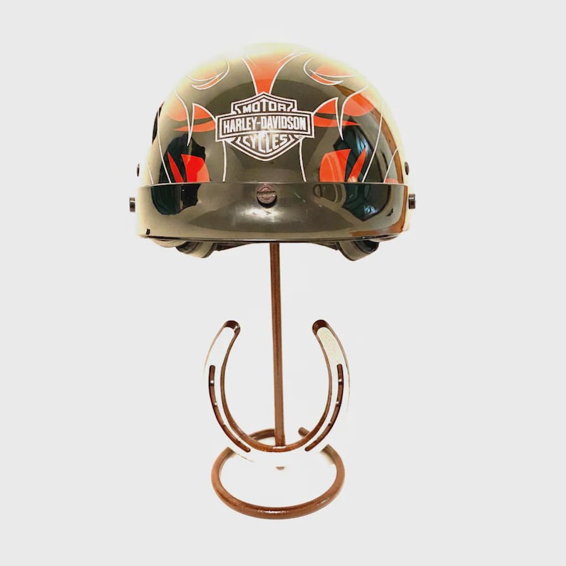 May include: A black Harley-Davidson motorcycle helmet with red and orange flame designs, displayed on a brown metal stand with horseshoe accents. The helmet features the Harley-Davidson Cycles logo.