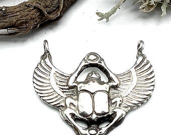 May include: A silver-toned metal pendant shaped like a winged scarab beetle. The design features a central beetle body with detailed, outstretched wings on both sides and two small loops at the top for attachment to a chain or cord.