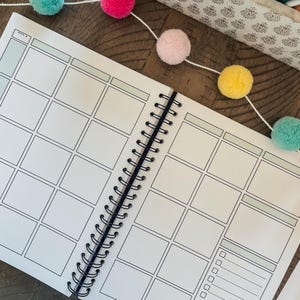May include: A white planner with a black spiral binding. The planner has a grid layout with blank squares for writing. The planner has the word "week" written at the top.