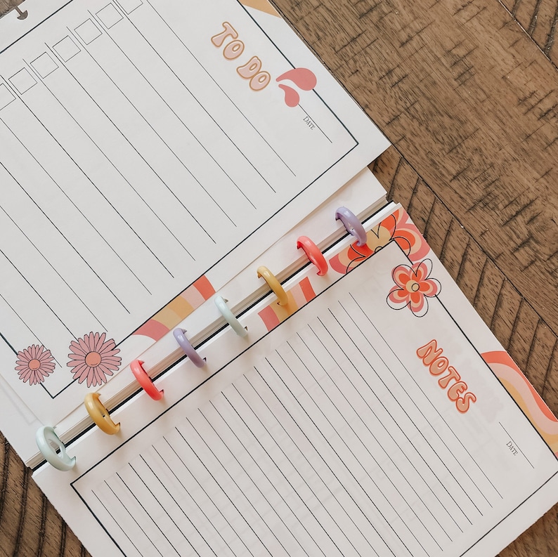 May include: A white planner with a to-do list and notes section. The planner has a colorful floral design and a date section. The planner is bound with colorful rings.