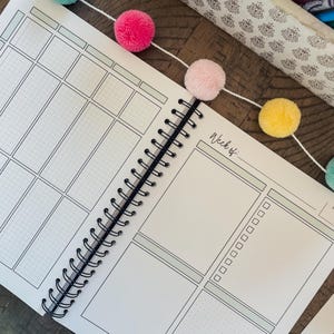 May include: A white planner with a black spiral binding. The planner has a gridded section on the left side and a blank section on the right side. The right side has the text "Week of:" at the top.