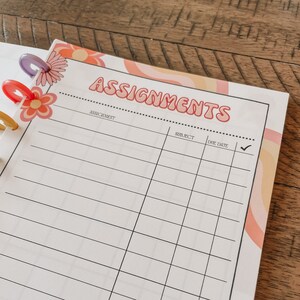 May include: A white planner page with a colorful design featuring pink, orange, and yellow swirls. The page is titled "Assignments" and has columns for "Assignment", "Subject", "Due Date", and a checkmark.