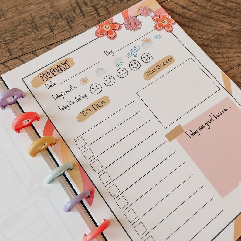May include: A white planner page with a rainbow design. The page has sections for the date, today's weather, how you're feeling, a to-do list, and a daily doodle. The page also has a pink sticky note with the text "Today was great because..."