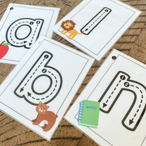 May include: Four white cards with black outlines, each featuring a different letter of the alphabet with numbered arrows indicating the tracing order. The letters are 'a', 'b', 'l', and 'h'. Each card has a small animal illustration at the bottom: an apple, a bear, a lion, and a notebook.