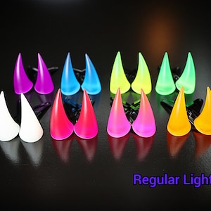May include: A collection of colorful, horn-shaped hair accessories in various shades including purple, blue, white, red, pink, yellow, and green. Each pair is attached to a black clip. The text "Regular Light" is visible at the bottom.
