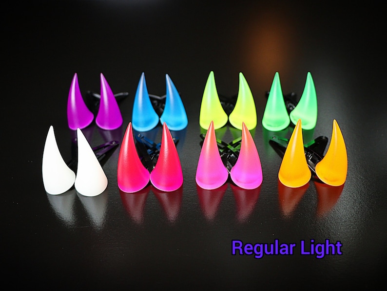 May include: A collection of colorful, horn-shaped hair accessories in various shades including purple, blue, white, red, pink, yellow, and green. Each pair is attached to a black clip. The text "Regular Light" is visible at the bottom.