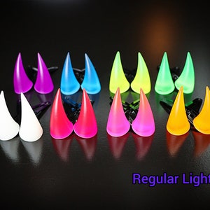 May include: Set of 10 pairs of glow-in-the-dark devil horns, in various colors including white, pink, blue, green, yellow, and orange. The horns are made of plastic and have a clip on the back for attaching to hair.