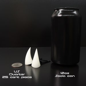 May include: A black soda can, two white cone-shaped objects, and a U.S. quarter are displayed on a black surface. The soda can is labeled "12oz Soda can". The quarter is labeled "U.S. Quarter 25 cent piece".