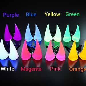 May include: A collection of glowing, horn-shaped hair clips in various colors, including purple, blue, yellow, and green. The image also displays white, magenta, pink, and orange clips. The text above each color indicates the color of the clip.