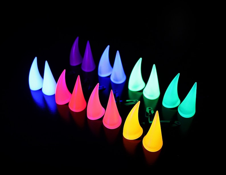 May include: A collection of glowing, horn-shaped accessories in a variety of colors, including white, pink, orange, yellow, green, and purple. The horns are arranged on a black surface, creating a vibrant and eye-catching display.
