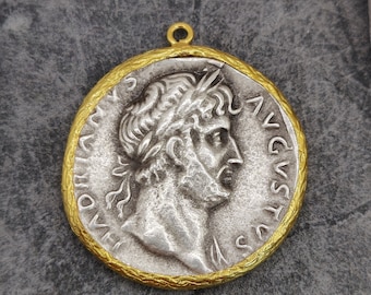 May include: A silver pendant with a gold rim, featuring a profile of a Roman emperor with a laurel wreath. The pendant has the inscription "IMP AVG" around the edge.