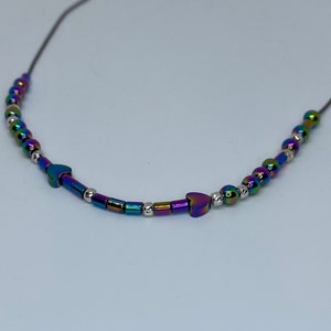 May include: A necklace with iridescent rainbow colored beads and silver beads. Two heart-shaped beads are in the center of the necklace.