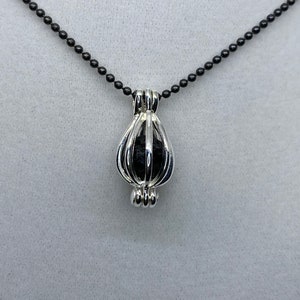 May include: A silver cage pendant necklace with a black stone inside. The necklace has a black chain.