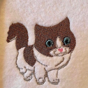 May include: Embroidered brown and white kitten with blue eyes and a pink nose. The kitten is walking with its tail curled up.