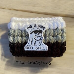 May include: A crocheted coffee cup cozy in white, gray, and black with an embroidered ghost wearing sunglasses and the text "This is some boo sheet".