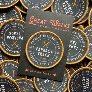 May include: A collection of circular sew-on patches and a card. The patches are dark green with gold trim and feature text and a crossed pickaxe design. The card reads "Great Walks Aotearoa New Zealand" and "Paparoa Track 55 KM".