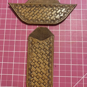May include: Two pieces of handcrafted leather, one rectangular and one boat-shaped, both featuring a basketweave pattern and decorative shell-like edges. The leather is a warm, golden brown color.