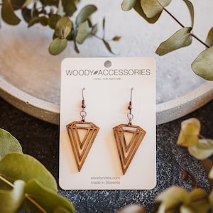 Op de afbeelding: Een paar houten oorbellen met een geometrische diamantvorm. De oorbellen zijn bruin en hebben een gelaagd ontwerp. De oorbellen worden getoond op een witte kaart met de tekst "Woody Accessories - Feel the Nature" en "woodynote.com made in Slovenia".