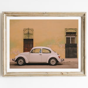 May include: A white vintage Volkswagen Beetle parked in front of a yellow building with two iron gates. The car is facing the right side of the image.