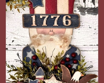 May include: A wooden patriotic Uncle Sam figurine with a red, white and blue top hat, a white beard, and a blue and white striped shirt. The figurine is holding a basket with red berries, green leaves, and a wooden eagle. The basket is decorated with stars and the number 1776.