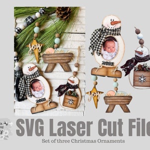 May include: Set of three laser cut Christmas ornaments.  The ornaments are made of wood and feature a snowman, a manger scene, and a star.  Each ornament has a space for a photo.  The ornaments are painted in a rustic style with black and white checkered accents.