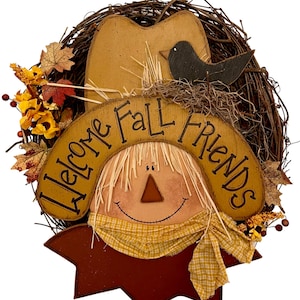 Peut inclure: Une couronne d'automne avec un visage de  épouvantail, un oiseau et les mots "Welcome Fall Friends" sur un fond en bois brun.