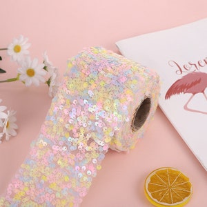 May include: A roll of iridescent pastel pink, yellow, and blue sequins on a mesh backing. The sequins are small and round.