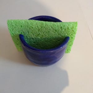 May include: A blue ceramic sponge holder with a green sponge inside.