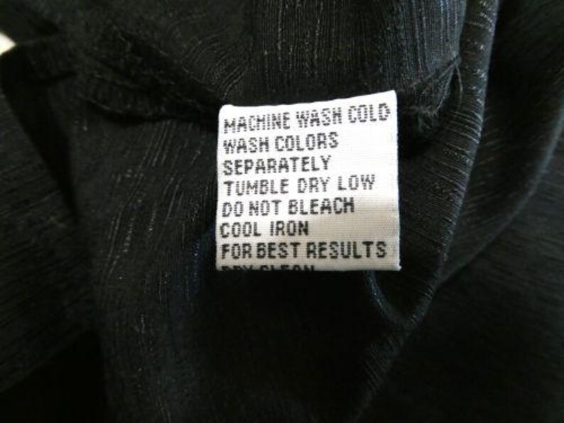 May include: Close-up of a black garment with a white care label. The label reads "MACHINE WASH COLD, WASH COLORS SEPARATELY, TUMBLE DRY LOW, DO NOT BLEACH, COOL IRON, FOR BEST RESULTS."