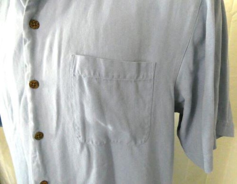 May include: A light blue short-sleeved button-down shirt with a single chest pocket.