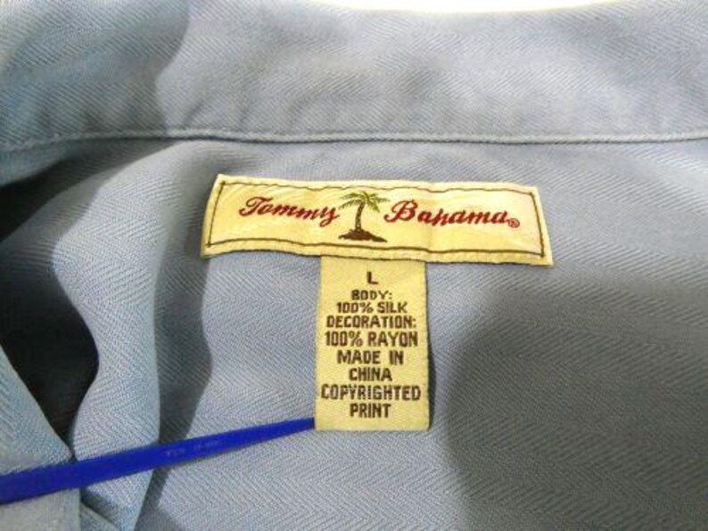 May include: A light blue button-down shirt with a Tommy Bahama label. The label states that the shirt is made of 100% silk and the decoration is 100% rayon. The shirt was made in China.