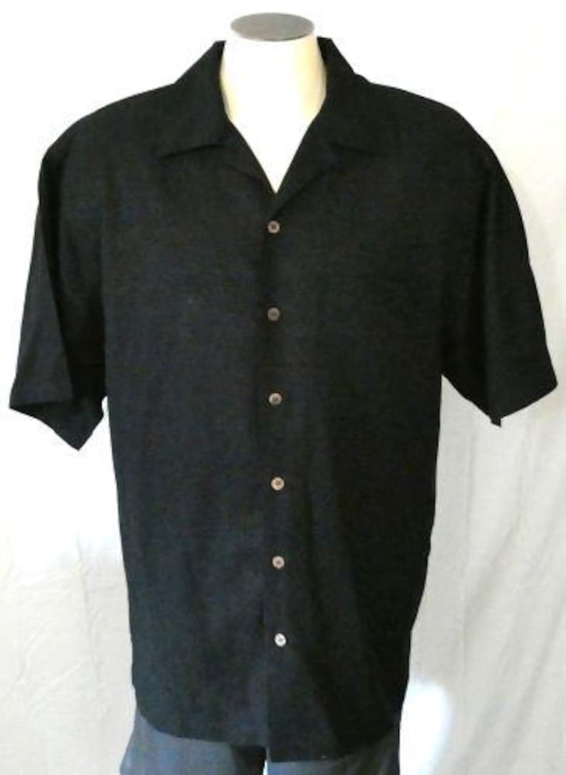 May include: Black short-sleeved button-down shirt with a classic collar. The shirt has a subtle textured pattern and is buttoned up the front with six buttons. The shirt is displayed on a mannequin.