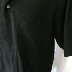 May include: Black short-sleeved shirt with a button-down collar and a single chest pocket. The shirt has a textured appearance and a button closure. The fabric appears to be a lightweight material.