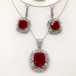May include: A ruby and diamond jewelry set featuring a pendant necklace, earrings, and a ring. Each piece has a square-shaped ruby surrounded by a delicate, ornate, silver setting with smaller diamonds.
