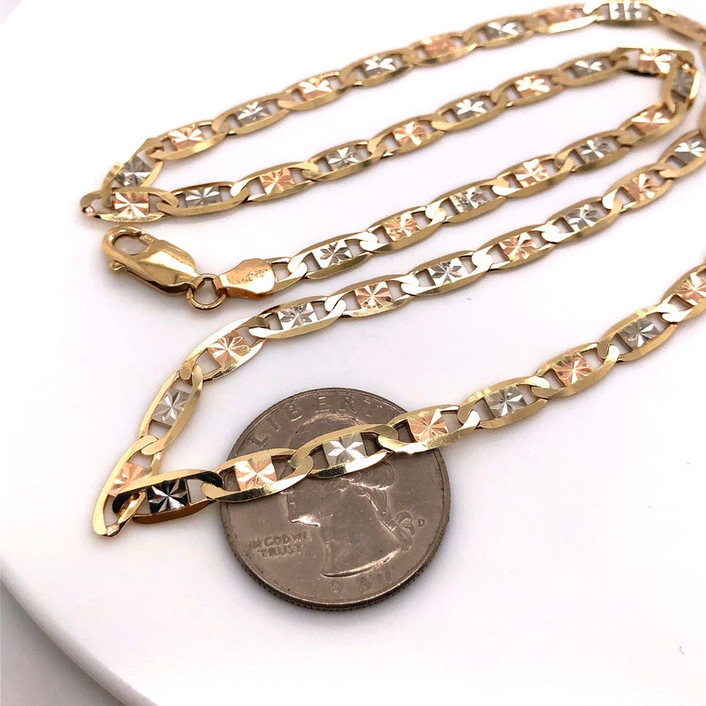 May include: A gold chain necklace with a mariner link design. The chain is made of three different colors of gold: yellow, white, and rose. The chain is lying on a white surface next to a US quarter.