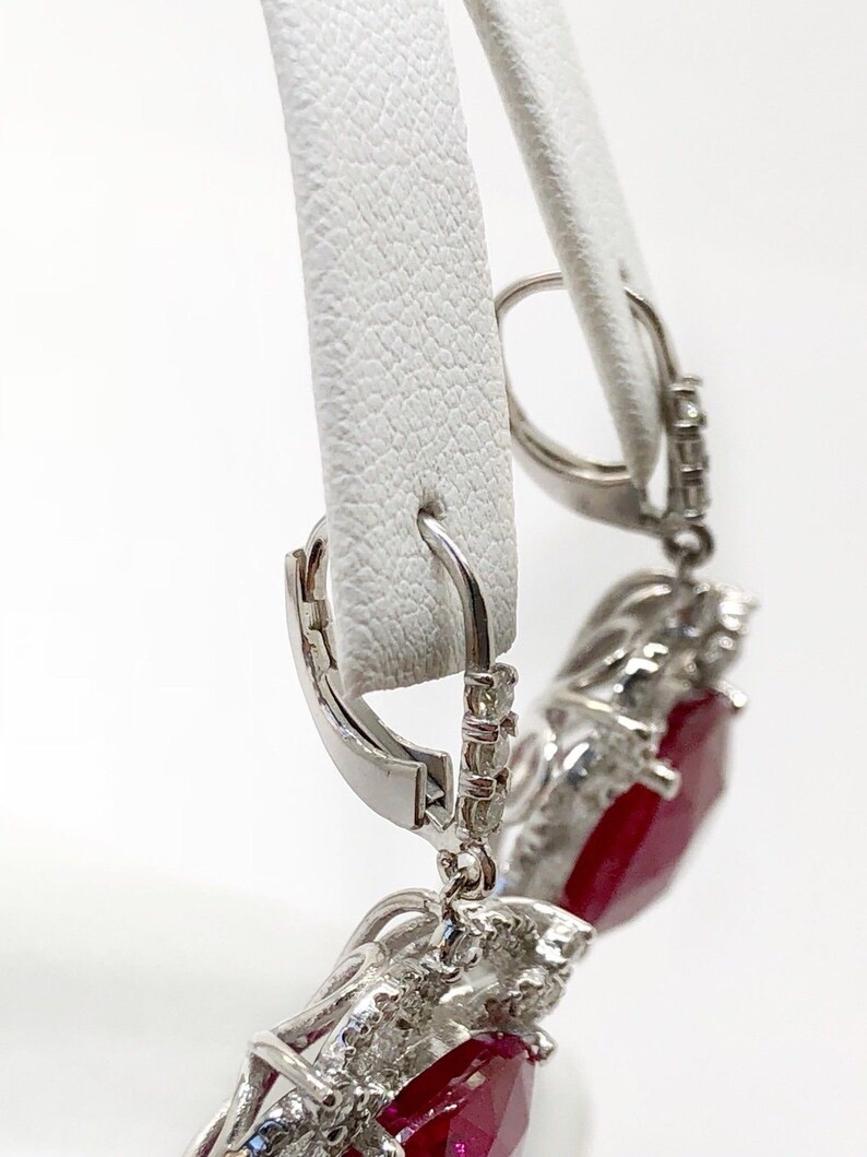 May include: A pair of dangle earrings with a large red gemstone surrounded by smaller white gemstones. The earrings have a silver hook closure.