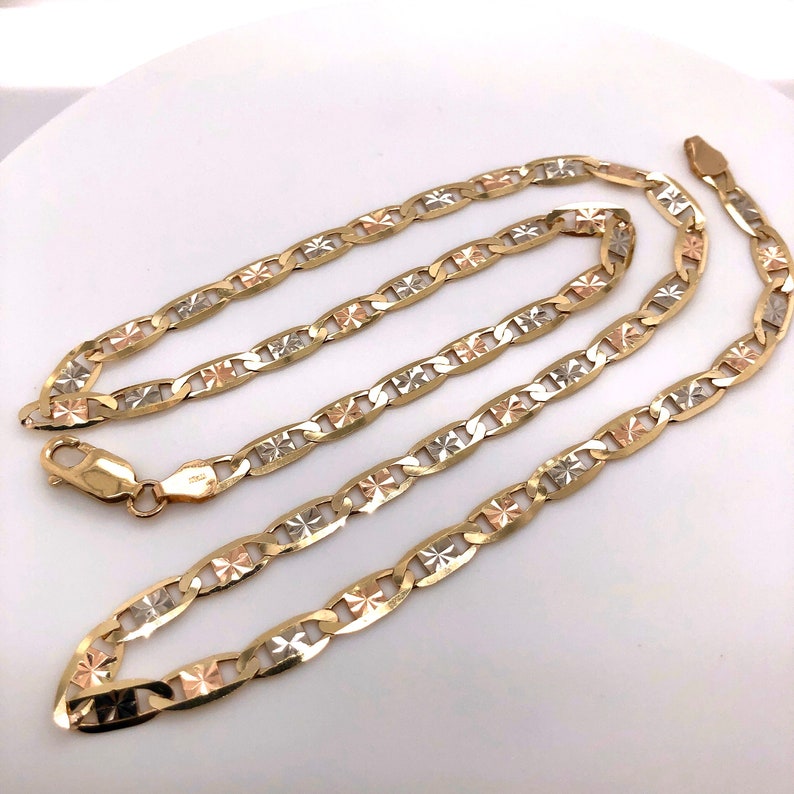 May include: A gold, silver, and rose gold chain necklace with a mariner link design. The chain has a diamond-shaped pattern on each link.