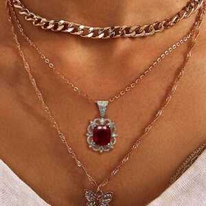 May include: A layered gold necklace set with a large red gemstone pendant and a smaller butterfly pendant.