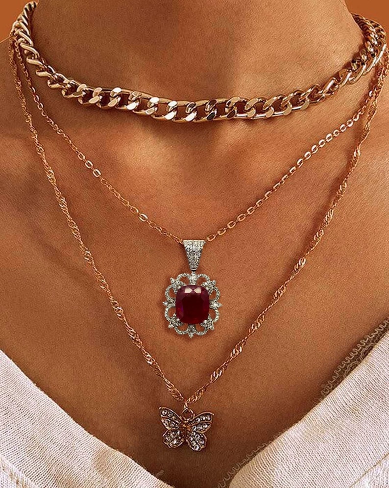 May include: A layered gold necklace set with a large red gemstone pendant and a smaller butterfly pendant.