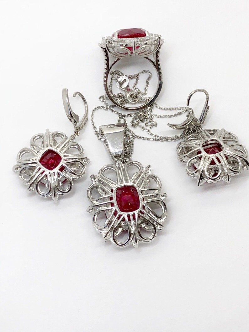 May include: A set of ruby and diamond jewelry featuring a ring, a pendant, and earrings. The pieces are all made of silver and feature a delicate, intricate design.