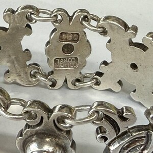 K&ouml;nnte beinhalten: Nahaufnahme eines Silberarmbands mit verzierten, stilisierten floralen und scrollartigen Gliedern. Das Armband ist durch kleine, runde Kettenglieder verbunden. Der Verschluss ist mit "925" und "TAXCO MEXICO" gestempelt.