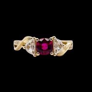 May include: A gold ring featuring a red gemstone and two smaller white gemstones. The ring has a twisted band.